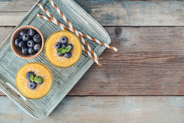 Refreshing and healthy mango smoothie in glasses with coconut flakes and fresh blueberries - 764037403
