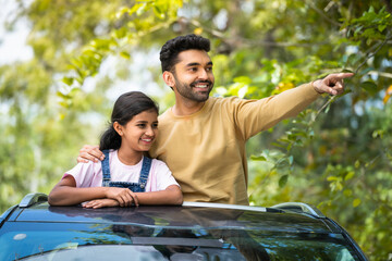 Happy indian father showing nature to daughter on car sunroof - concept of vacation, traveling and...