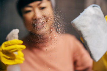 Close up of an asian woman spraying detergent on a glass and cleaning it.