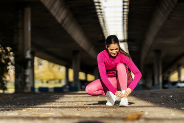 A sportswoman in shape is tying her shoelace.