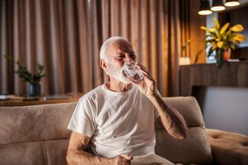 An ill senior man is drinking water and refreshing himself.