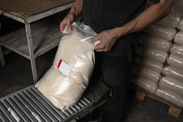 An employee in a dirty workshop is engaged in packing food, takes a full bag of sugar from the...