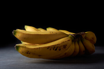 bunch of fresh bananas, ripe tropical fruit with bright yellow peel and deliciously sweet flavor, on dark textured surface with isolated on black background, selective focus with copy space - Powered by Adobe