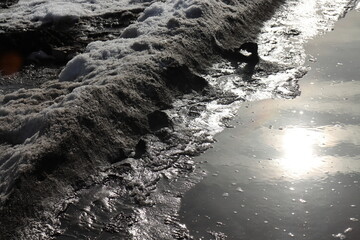 Reflection of the sun on dirty water puddles from melting snow in spring