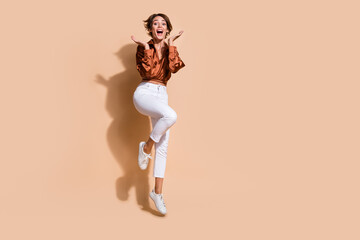 Fototapeta na wymiar Full length photo of shocked funky lady dressed brown top jumping high rising arms empty space isolated beige color background