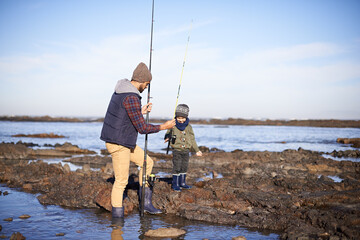 Father, boy and fishing at sea in winter as hobby with bonding for child development, learning and growth in Australia. Dad, kid and stand in boulders at coast for family tradition, memory and care