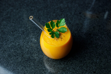 Mango Carrot Apple Smoothie in a glass on dark background with glass straw