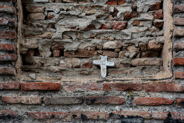 A small, white cross embedded in a crumbling brick wall in Tbilisi, Georgia.
