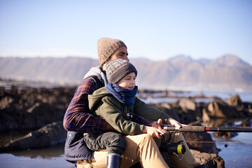 Father, fishing and young boy on rocks, teaching and bonding for activity by ocean. Sea, rod and...