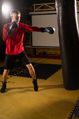 Young man training boxing in the punching bag in gym. Sport, boxing and training