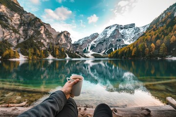 A first-person perspective of a hand holding a mug with a stunning mountain lake landscape in the background, evoking peace