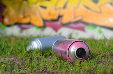 Several used spray cans with paint and caps for spraying paint under pressure on grass near the...