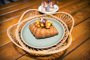 Caramel macadamia croissant decorated with flowers in a blue ceramic dish in rattan tray on a...