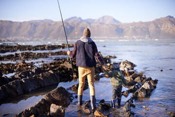 Man, kid and beach for fishing in winter as hobby with bonding for child development, growth and life skills in Australia. Dad, boy and stand in rocks at coast for family tradition, memory and care - obrazy, fototapety, plakaty