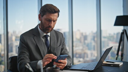 Serious professional using smartphone in modern office. Company leader typing