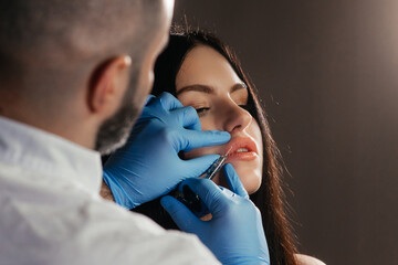 The doctor cosmetologist makes Lip augmentation procedure of a beautiful woman in a beauty...