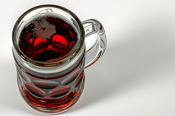 Mug of dark red beer, on a white surface.