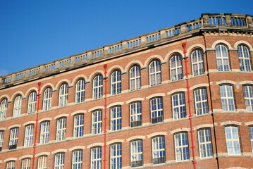 Fototapeta na wymiar Facade of Renovated 19th Century Cotton Spinning Mill seen against Blue Sky 