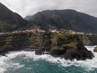 Aerial view of Seixal, a little village by the ocean with waves and surrounded with incredible mountains on the island of Madeira, Portugal.