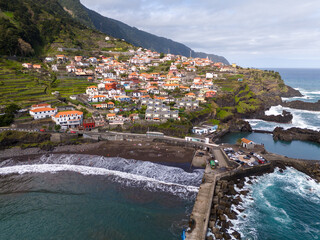 Aerial view of Seixal, a little village by the ocean with waves and surrounded with incredible mountains on the island of Madeira, Portugal.