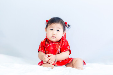 Chinese New Year concept, cute happy little girl in Chinese dress sitting in white living room. Cute Asian baby sitting in white living room, Chinese New Year concept.