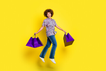 Full length photo of funky excited woman wear print shirt jumping high holding bargains isolated...