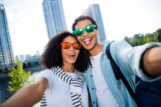 Selfie photographing young family couple wear casual outfit and sunglass stick tongue out for cadre with kyiv skyscrapers on background