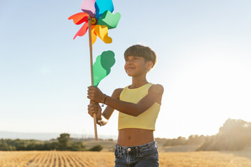 Cheerful short haired girl playing in nature in the park with colorful pinwheel toy.