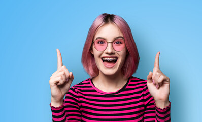 Excited pink woman in braces, opened mouth, wear sunglasses glasses spectacles advertise peeking...