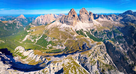 Ideal for poster: Panoramic, overall view of the Tre Cime mountain massif and the surrounding area from above. Beautiful autumn day, sunny, blue sky, sunlit mountains. Traveling Dolomites, Italy.
