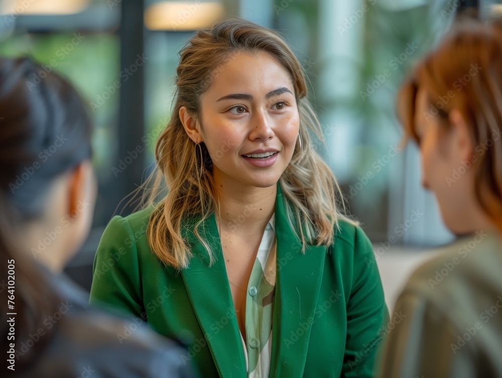 Wall mural A focused young woman in a stylish green blazer participates in an office meeting, her attention directed towards a colleague speaking off-camera.