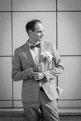 The groom in a wedding suit with a bow tie in a black and white photo adjusts his sleeve