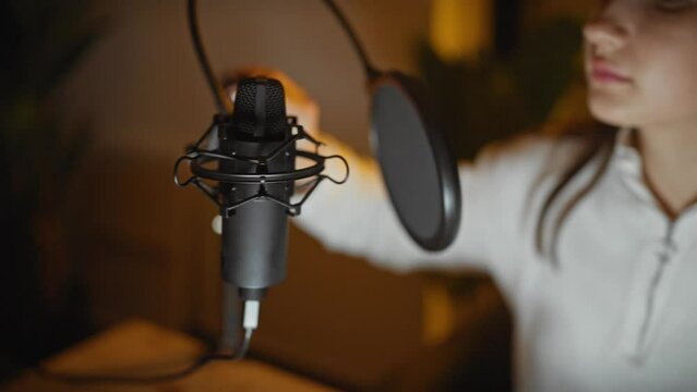 A young caucasian woman recording vocals in a well-equipped studio, displaying concentration and professionalism.