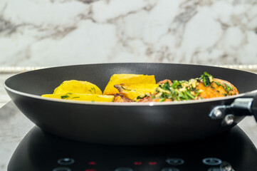 A black pan with a potatoes and meat in it. The vegetables include carrots and potatoes