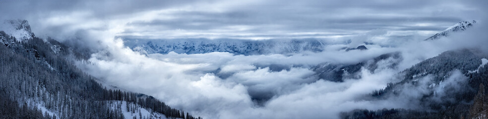 Winter in the mountains:  large Panorama of the Pale di San Martino valley, view from the air. Dramatic cloud cover, snow covered trees and surroundings. Italy, Dolomites, San Martino de Castrozza. 