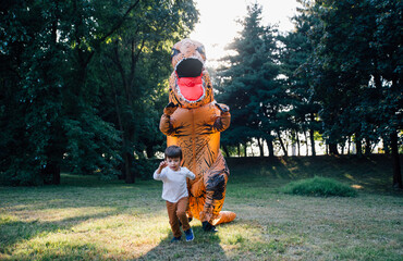 Father and son playing at the park, with a dinosaur costume, having fun with the family outdoor © oneinchpunch