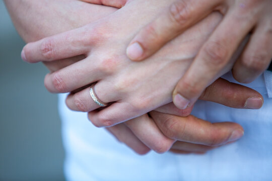 A close-up photograph capturing the delicate touch of a couple's hands clasped together, with a focus on a diamond ring that signifies a deep commitment. The image evokes a sense of intimacy and the