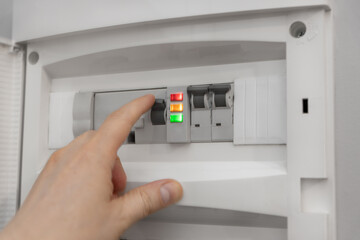 Skrzynka rozdzielcza elektryczna w mieszkaniu z palącymi się diodami. Dłoń trzymająca na przełączniku prądu, Wyłączenie prądu.  Koncept drożejącego prądu i z problemami w gospodarstwach domowych.