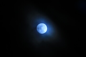 Bright blue moon in a black sky with clouds in the cold night