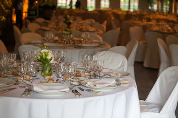 A view across a grand banquet hall adorned with multiple round tables set with white linens, sparkling glassware, and fine silverware. Each table is centered with a delicate floral arrangement