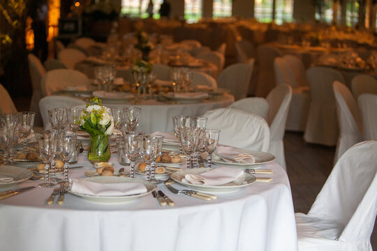 A view across a grand banquet hall adorned with multiple round tables set with white linens, sparkling glassware, and fine silverware. Each table is centered with a delicate floral arrangement