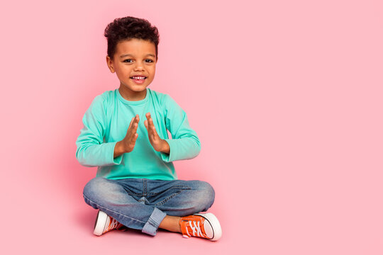 Full size photo of charming small boy sit floor clap hands applause dressed stylish cyan outfit isolated on pink color background