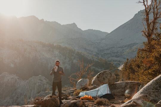 Camper drinking coffee at sunrise in the mountains