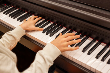 Close-up of a boy's hands on the keys of a piano, child learning to play piano - obrazy, fototapety, plakaty