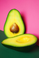 Halves of cut avocado on pink and green background