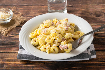 Traditional Italian recipe, creamy ham Tortellini on a white dish and wooden table.