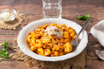 Traditional Italian dish, Tortellini with Bolognese sauce on a white plate and wood background.
