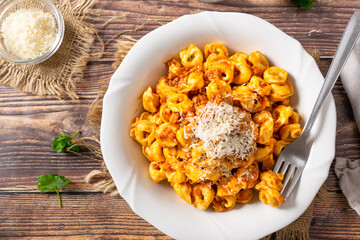 Traditional Italian dish, Tortellini with Bolognese sauce on a white plate and wood background.