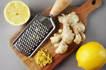 Whole and cut lemons next to ginger root and grater on a wooden board on a light background