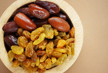 Dried dates and raisins in a wooden plate on a light background